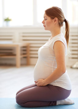 A pregnant person sitting on a exercise mat and doing mind body therapie.